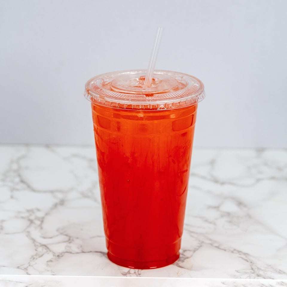 A vibrant red Mexican drink in a clear plastic cup with a straw on a marble surface.