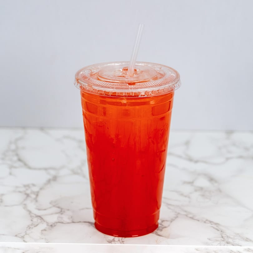 A vibrant red Mexican drink in a clear plastic cup with a straw on a marble surface.