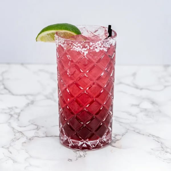 A vibrant red margarita in a textured glass with a salted rim, lime wedge, and straw.