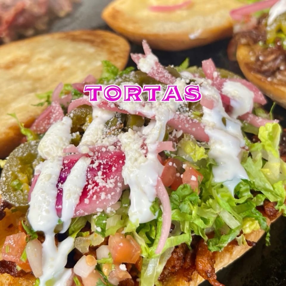 Close-up of a Mexican torta with lettuce, tomatoes, pickled onions, jalapeños, and crema.