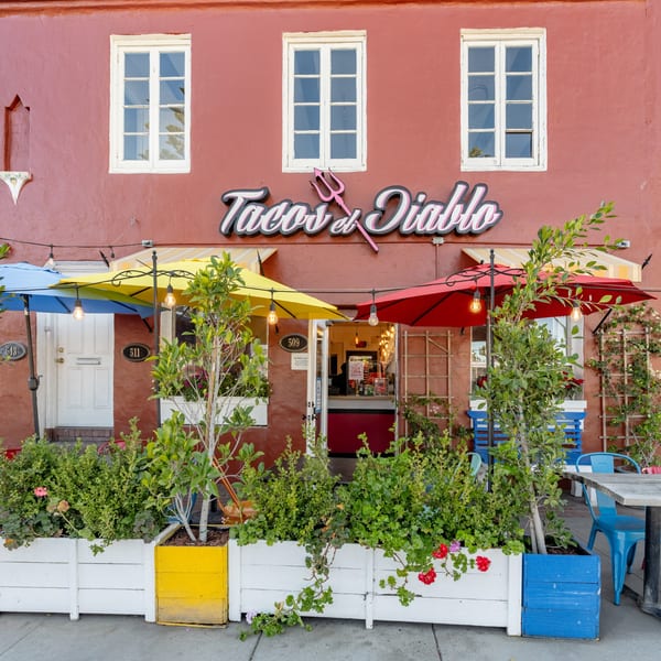 The vibrant red exterior of Taco el Diablo, with colorful umbrellas, planters, and outdoor seating.