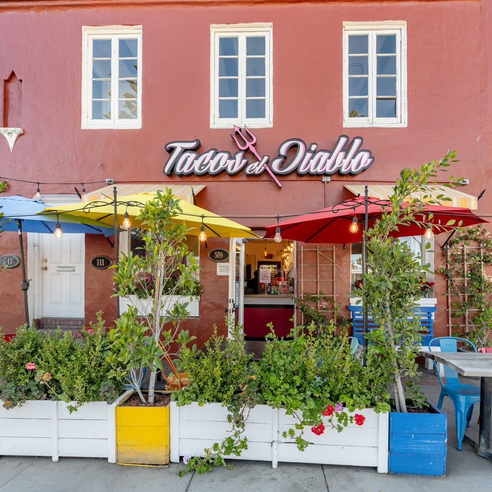 The vibrant red exterior of Taco el Diablo, with colorful umbrellas, planters, and outdoor seating.