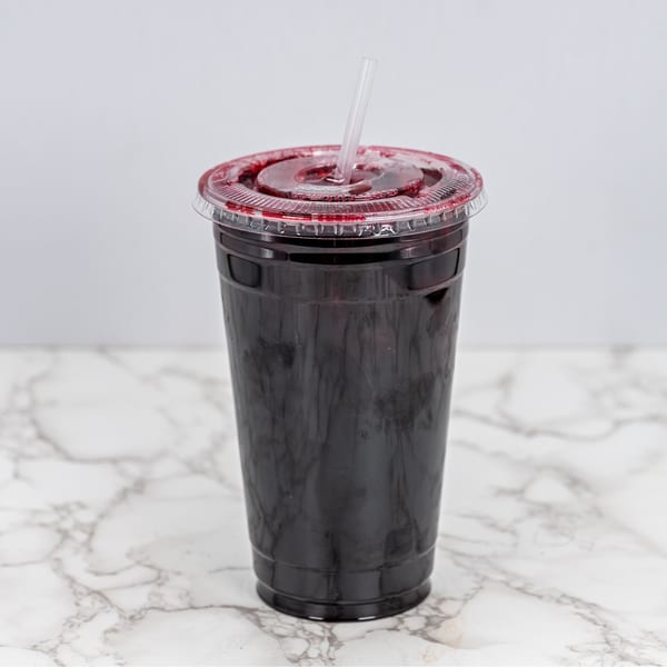 Dark red Mexican drink in a clear plastic cup with a straw on a marble surface.
