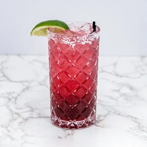 A vibrant red margarita in a textured glass, garnished with a lime wedge and salt rim, on a marble surface.