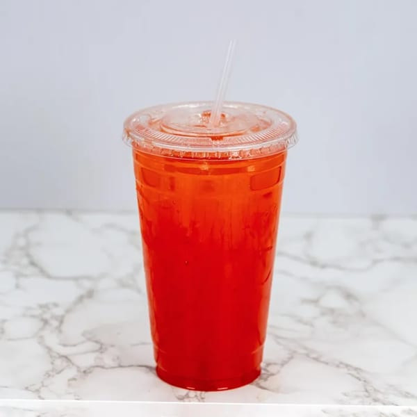 A vibrant red agua fresca in a clear plastic cup with a straw, on a marble surface.