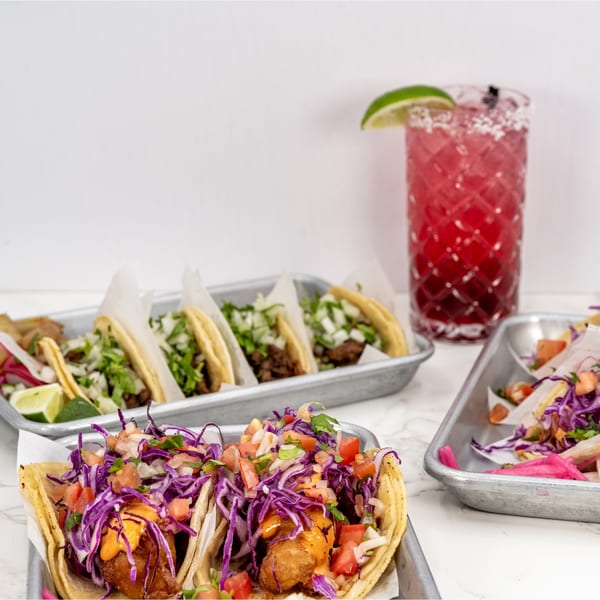 Assortment of Taco el Diablo tacos with various toppings and a red margarita on a white marble surface.