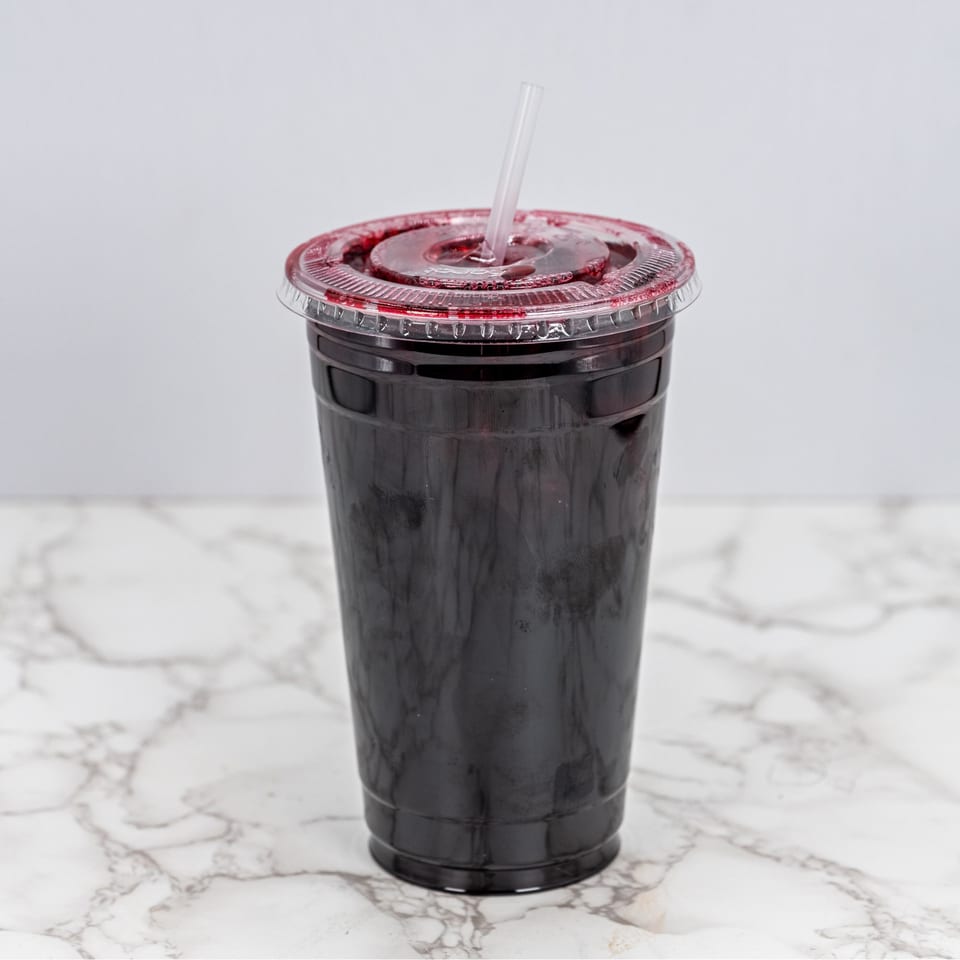 Dark red Mexican drink in a clear plastic cup with a straw on a marble surface.