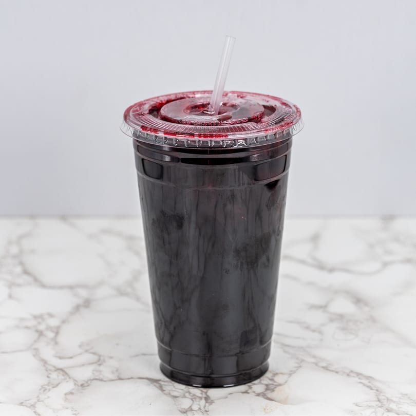 Dark red Mexican drink in a clear plastic cup with a straw on a marble surface.