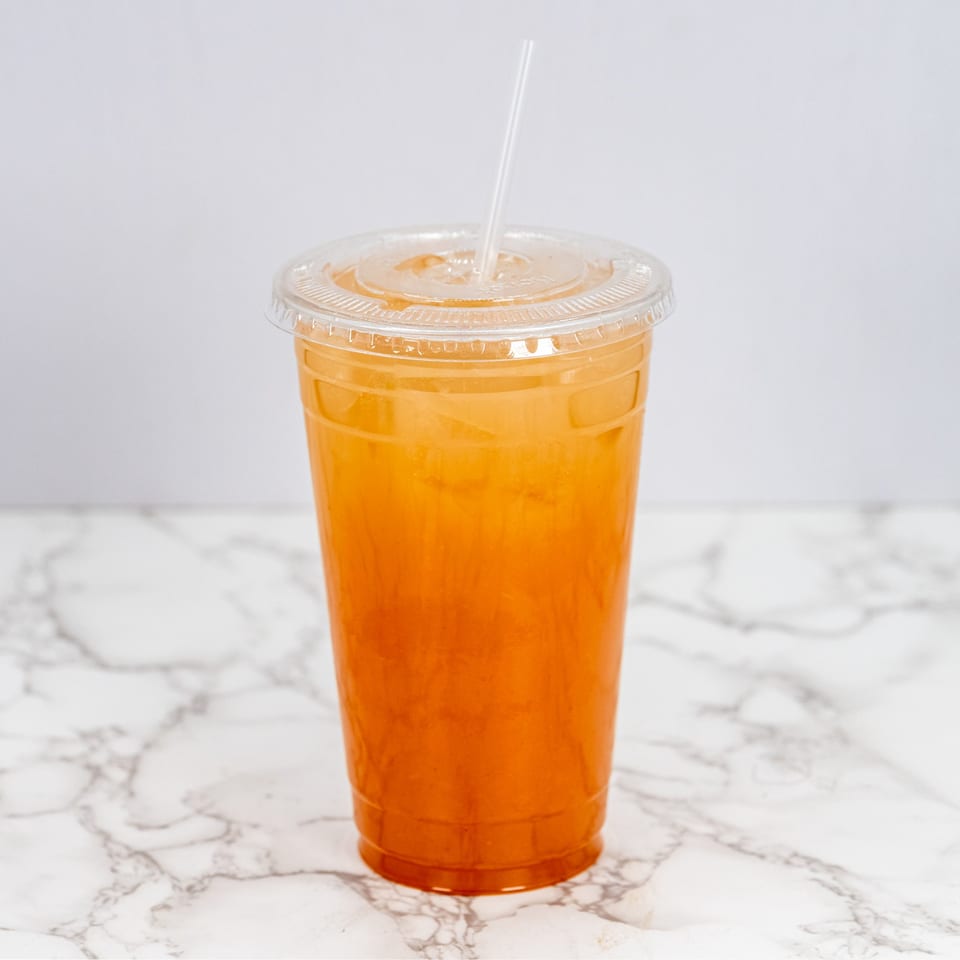 A clear plastic cup filled with a vibrant orange drink and ice, with a straw, on a marble surface.