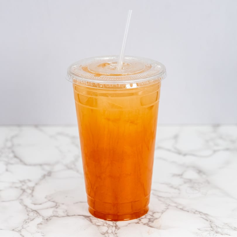 A clear plastic cup filled with a vibrant orange drink and ice, with a straw, on a marble surface.