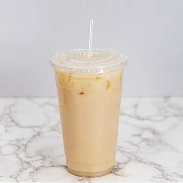 Iced horchata in a clear plastic cup with a straw on a marble surface.