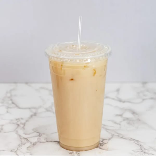 Horchata in a clear plastic cup with a lid and straw on a white marble surface.