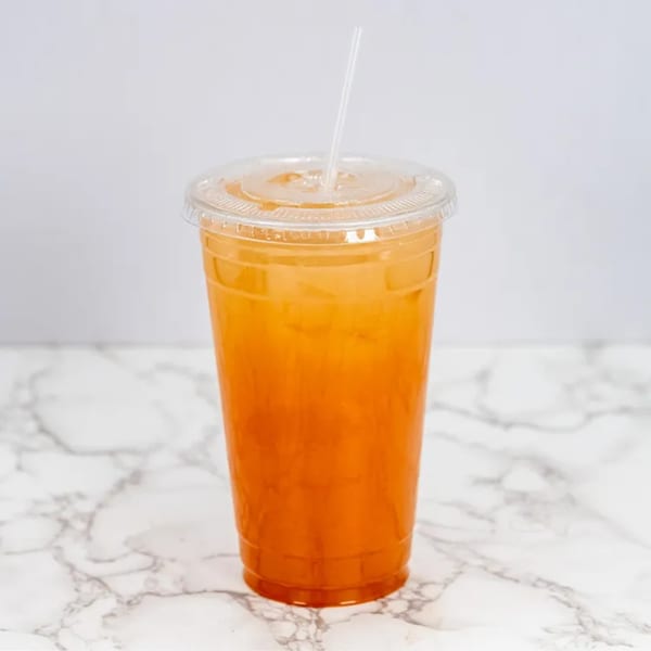 A vibrant orange drink with ice and a straw in a clear plastic cup on a marble surface.