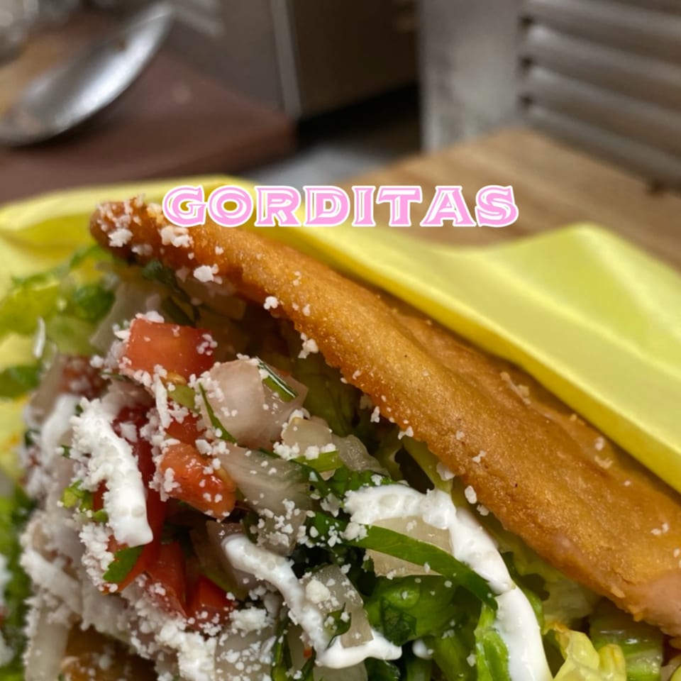 A close-up of a Taco el Diablo gordita, filled with lettuce, tomatoes, onions, crema, and cheese.