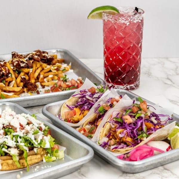 Mexican feast with tacos, loaded fries, a huarache, and a red margarita with a lime.
