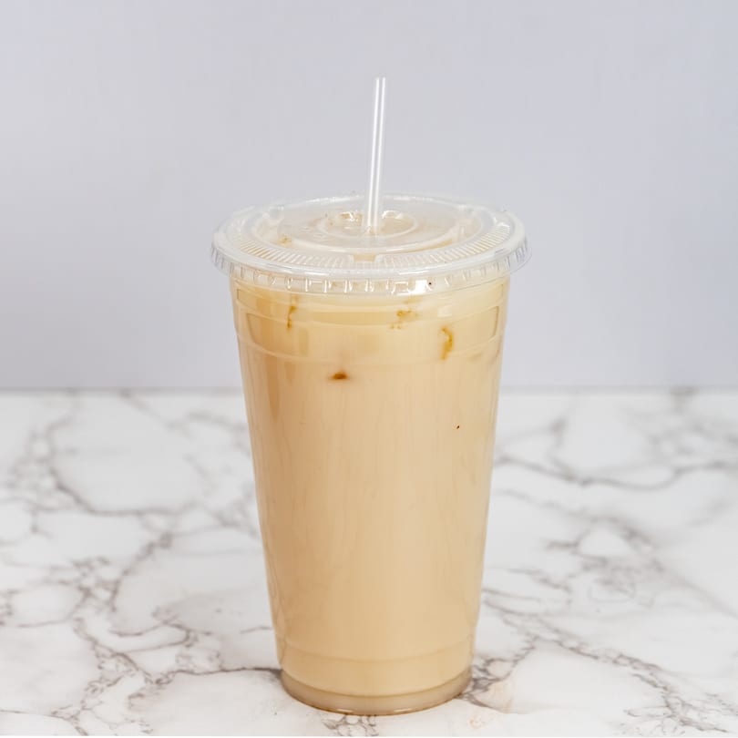 Iced horchata in a clear plastic cup with a straw on a white marble surface.