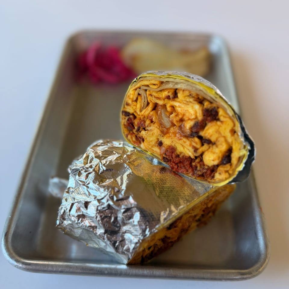 A cut burrito, filled with scrambled eggs and chorizo, wrapped in foil on a metal tray.