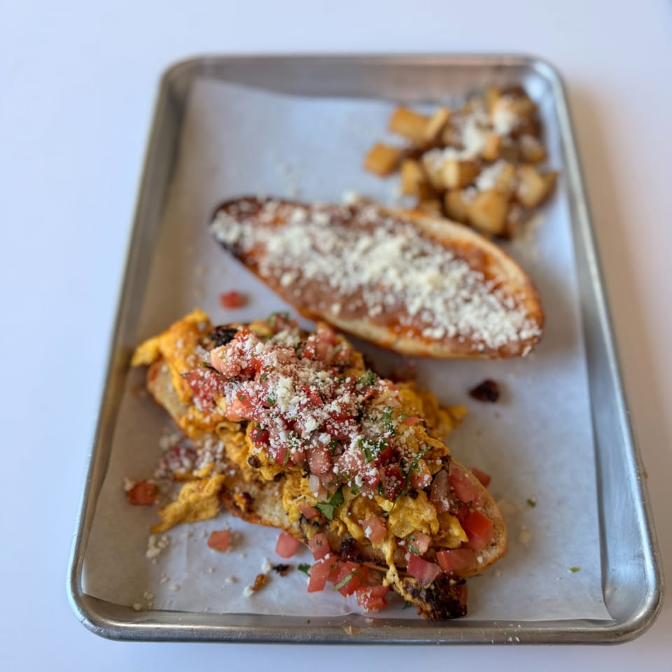 Mexican breakfast on a metal tray with scrambled eggs, pico de gallo, refried beans, and potatoes.