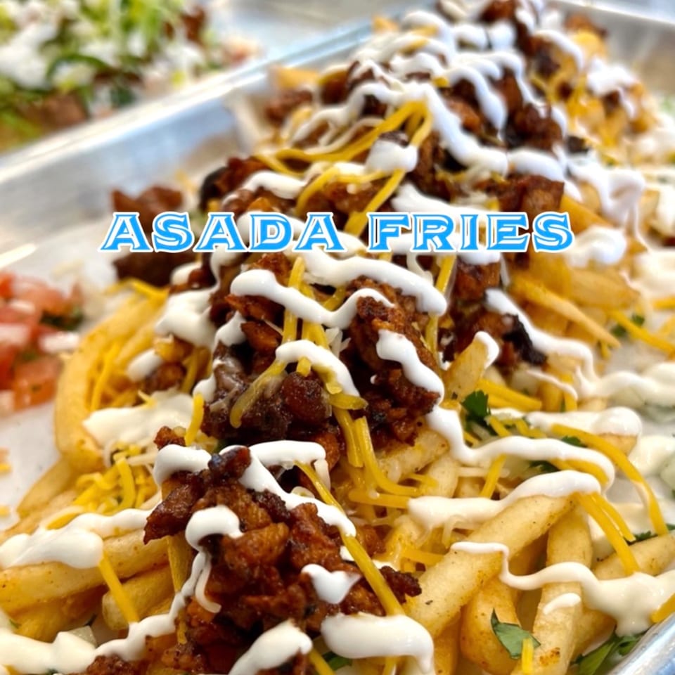 Close-up of golden Asada Fries topped with seasoned meat, shredded cheese, and white sauce.