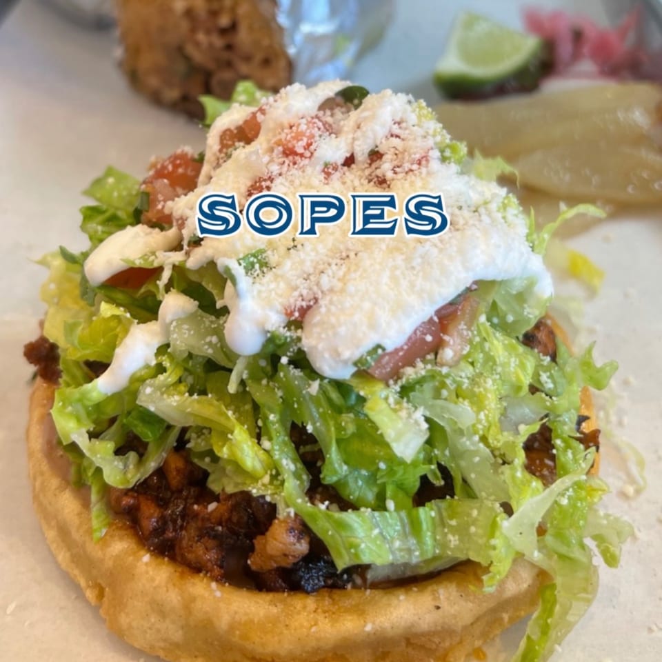 A close-up of a sopes from Taco el Diablo, topped with lettuce, sour cream, and cheese.