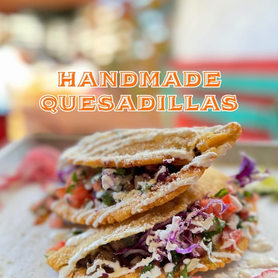 Two handmade quesadillas from Taco el Diablo, filled with meat, cabbage, tomatoes, and drizzled with cream.