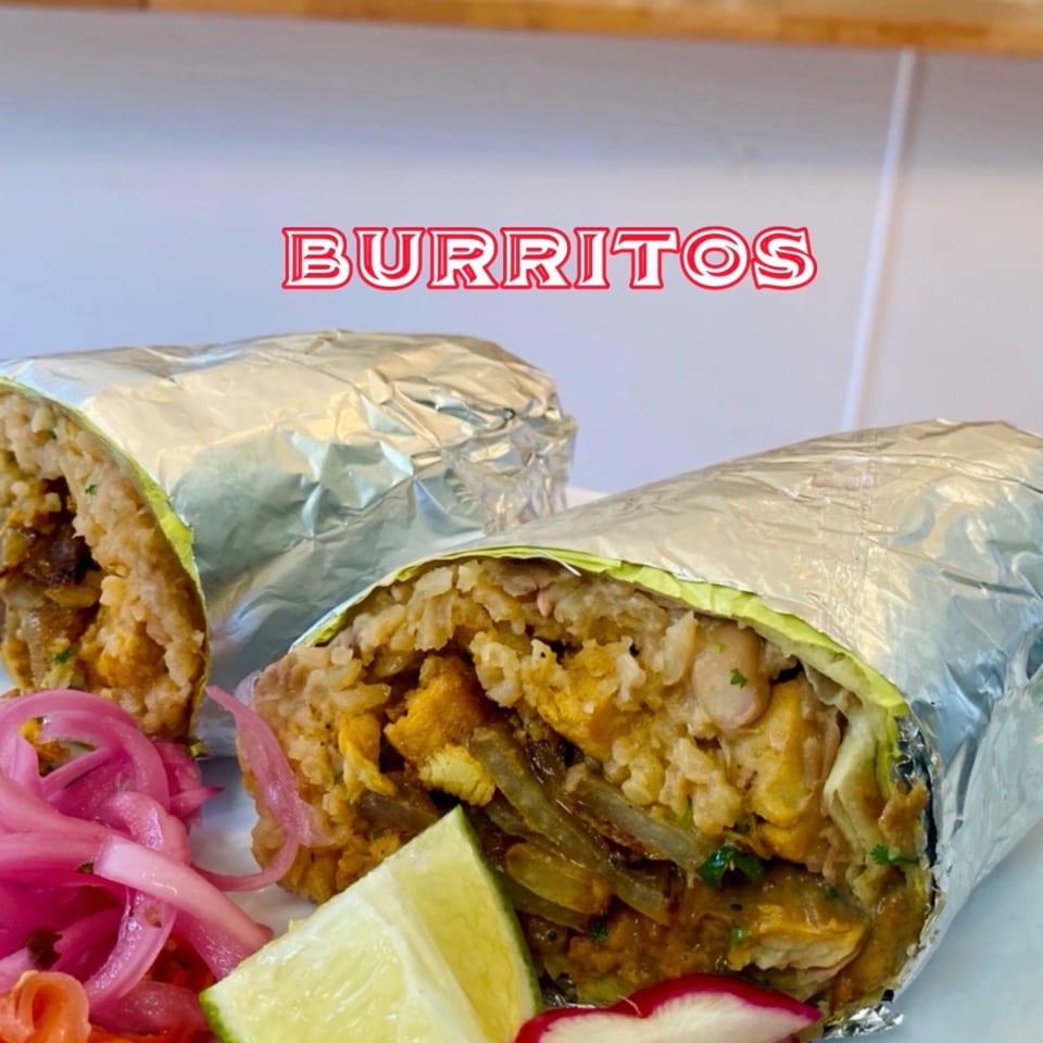 Two large burritos, partially unwrapped from foil, with rice, chicken, and pickled onions.