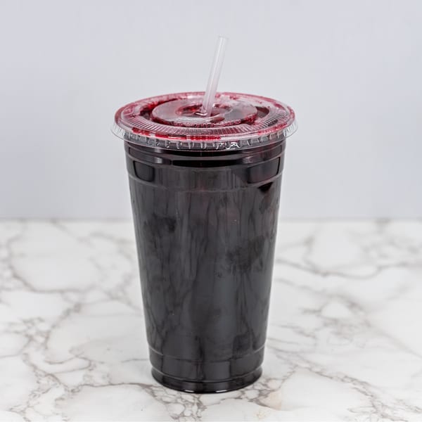 Dark red Mexican drink in a clear plastic cup with a straw on a marble surface.