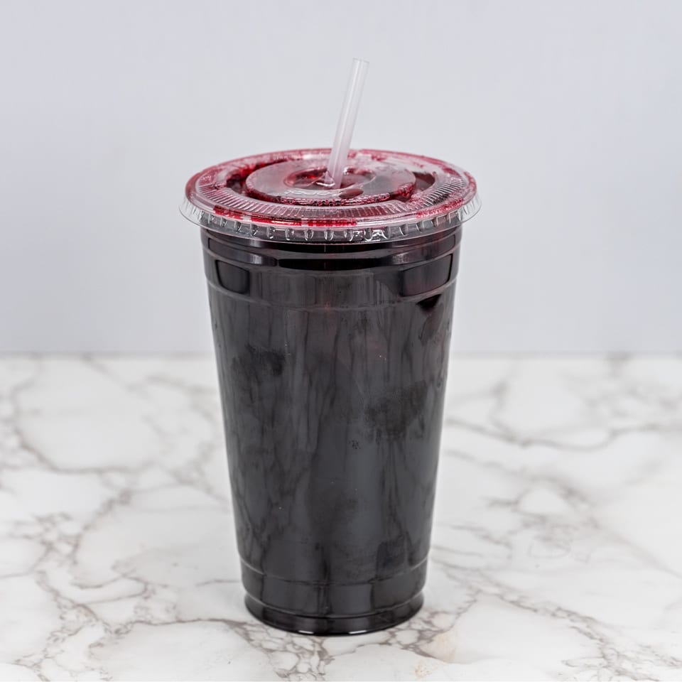 Dark red Mexican drink in a clear plastic cup with a straw on a marble surface.