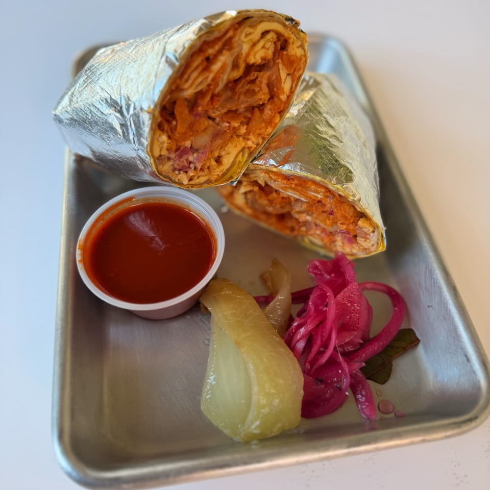 Two foil-wrapped burritos, red sauce, pickled onions, and a pepper on a metal tray.